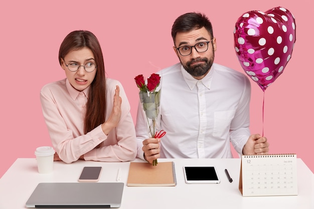 Partner bei der Arbeit klären Beziehungen. Unzufriedene Frau weigert sich, Blumenstrauß und Valentinstag von männlichem Kollegen zu erhalten, lehnt Werbung ab