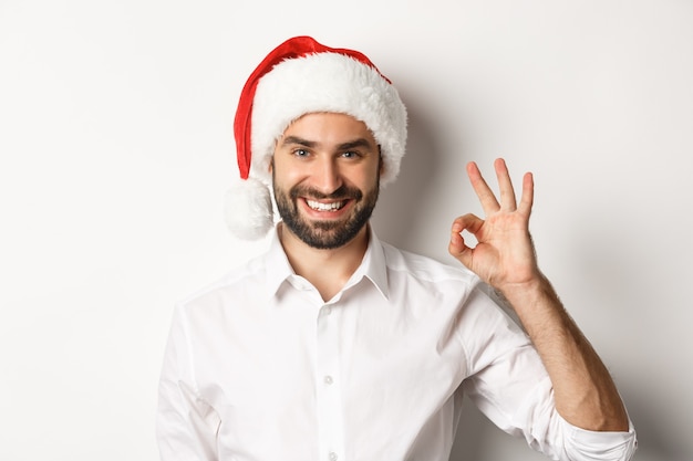 Party-, Winterferien- und Feierkonzept. Zuversichtlich Mann in Santa Hut zeigt okay Zeichen, genehmigen und mögen