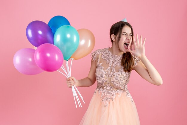Partygirl mit Partykappe schreien, während Luftballons auf rosa halten