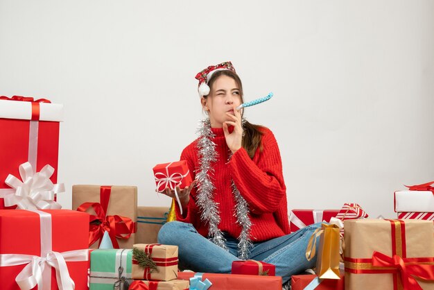 Partygirl mit Weihnachtsmütze hält Geschenk mit Krachmacher, der um Geschenke auf Weiß sitzt