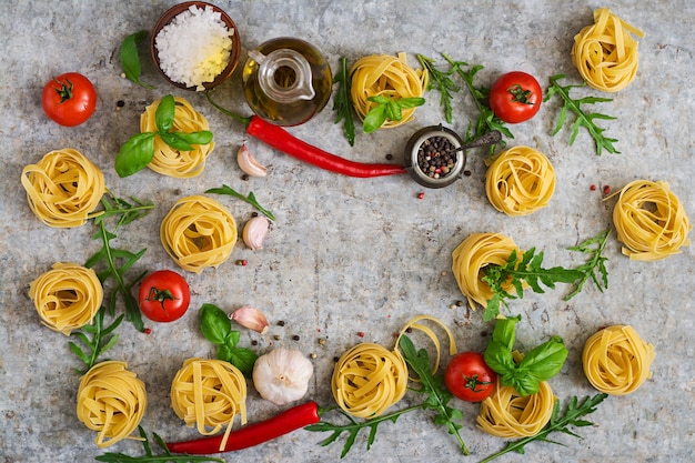 Pasta Tagliatelle Nest und Zutaten zum Kochen (Tomaten, Knoblauch, Basilikum, Chili). Ansicht von oben