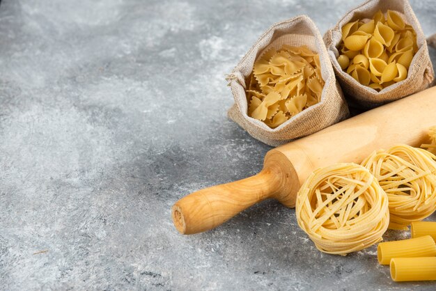 Pastasorten im rustikalen Korb mit einem hölzernen Rollrosa auf Marmortisch.