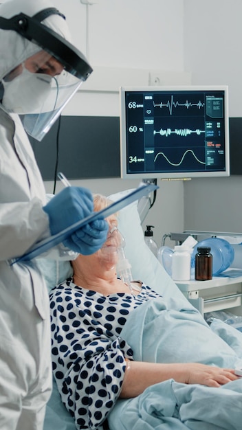 Patient mit Coronavirus spricht mit Arzt im Schutzanzug über Virusausbruch und Pandemie. Mediziner beraten Seniorin mit ansteckender Krankheit im Sperrbereich des Krankenhauses.