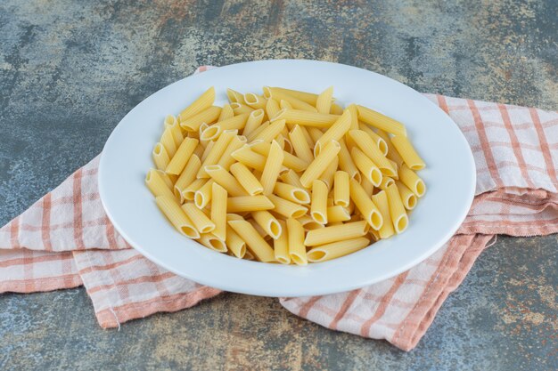 Penne Pasta auf dem Teller, auf dem Handtuch, auf dem Marmorhintergrund.