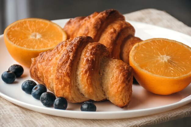 Perfektes Frühstück am Morgen - frische Croissants, Orangen und Blaubeeren auf einem Teller