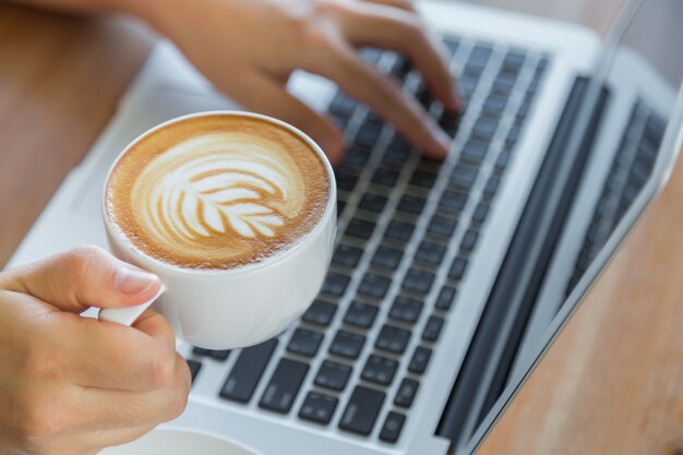 Person arbeitet an einem Laptop mit einer Tasse Kaffee neben