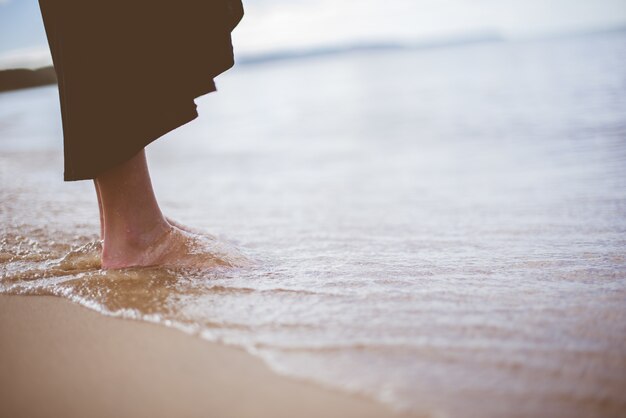 Person, die am Strandufer mit den Wellen steht, die zum Ufer kommen