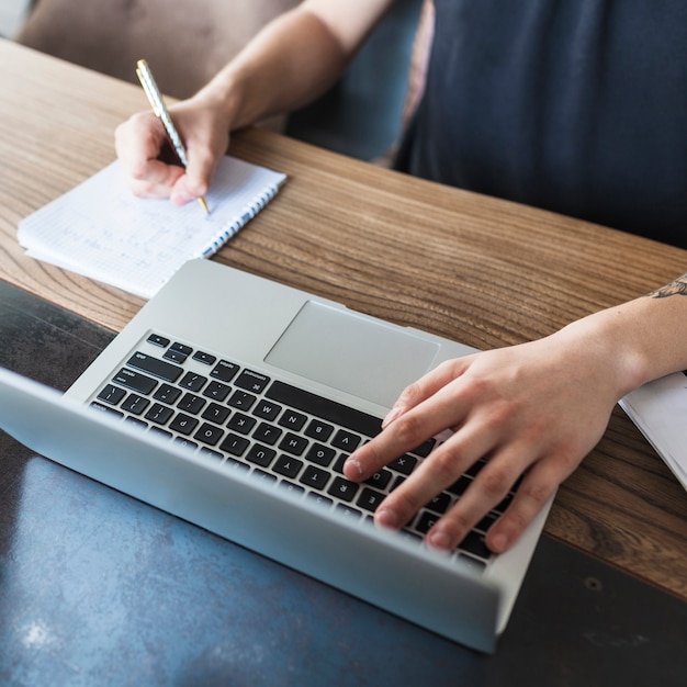 Person, die an Laptop am Holztisch arbeitet