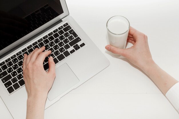 Person, die an Laptop nahe bei einem Glas Milch arbeitet