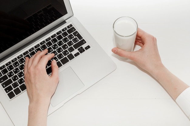 Person, die an Laptop nahe bei einem Glas Milch arbeitet