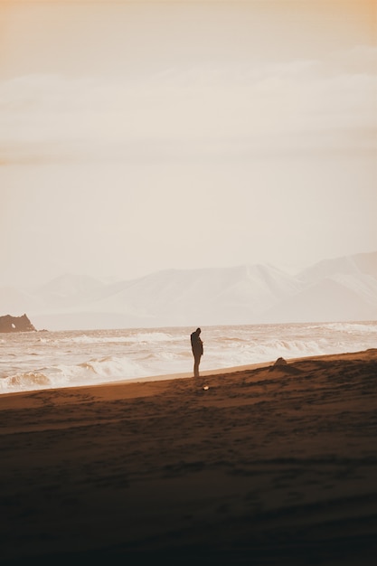 Person, die auf dem Sandstrand mit einem klaren weißen Himmel steht