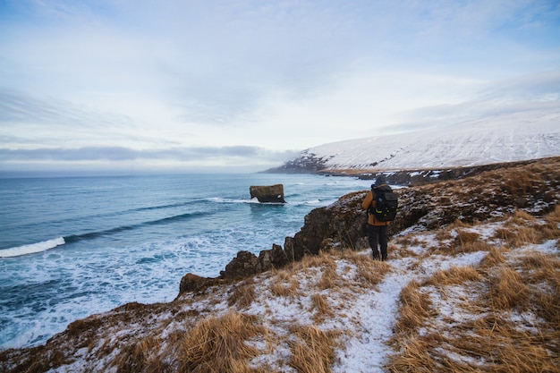 Person, die auf den Hügeln steht, die im Schnee bedeckt sind, umgeben vom Meer in Island