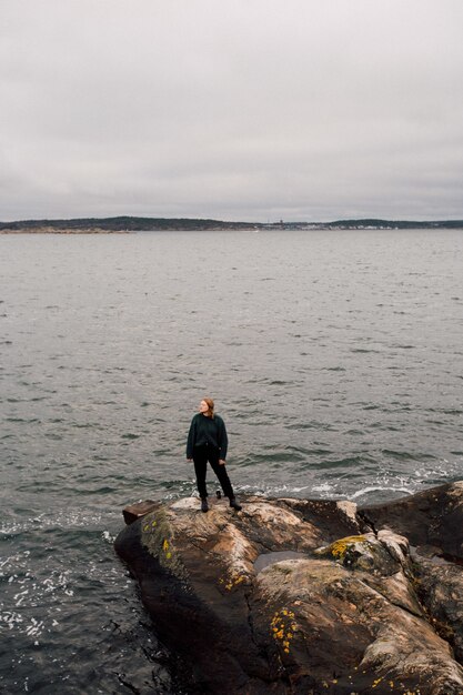 Person, die auf einem Felsen am Meer steht und zur Seite schaut