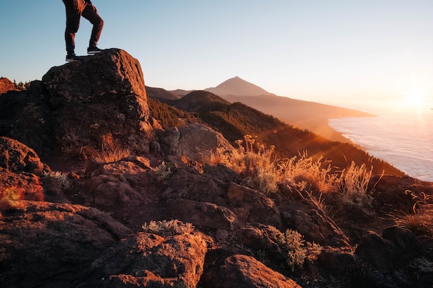 Person, die bei einem hellen Sonnenuntergang auf einem vom Meer umgebenen Felsen steht - Erfolgskonzept