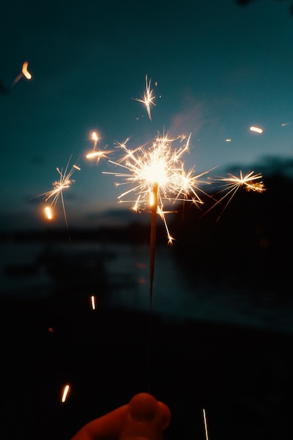 Person, die bengalische Lichter oder Wunderkerzen auf einem dunklen verschwommenen Hintergrund hält