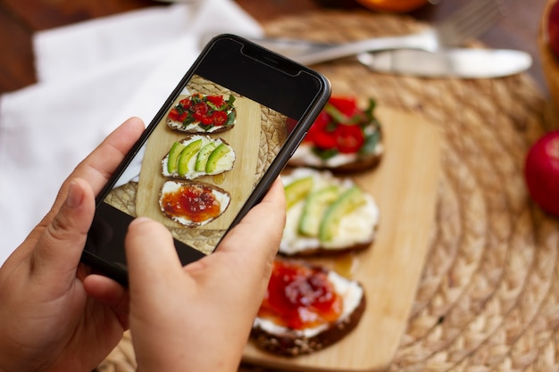 Kostenloses Foto person, die ein sandwich-sortiment mit smartphone fotografiert