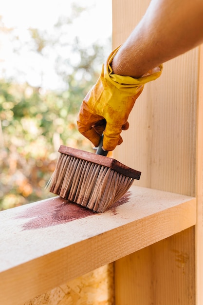 Person, die ein Stück Holz vom Hausbau lackiert