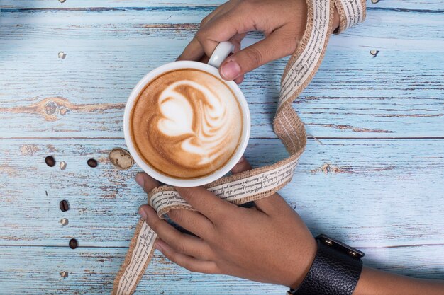 Person, die eine Tasse milchigen Kaffee mit zwei Händen hält