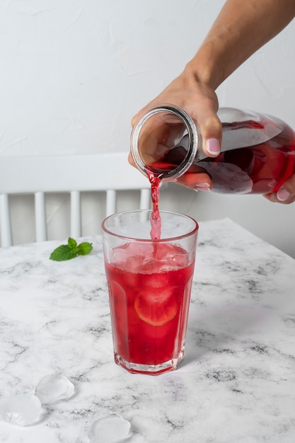 Person, die erfrischenden Hibiskus-Eistee in einen durchsichtigen Glasbehälter gießt