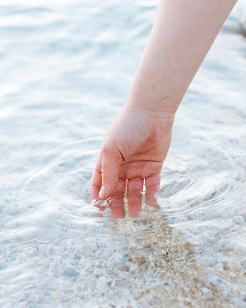 Person, die ihre Hände in klares Wasser mit Sand legt