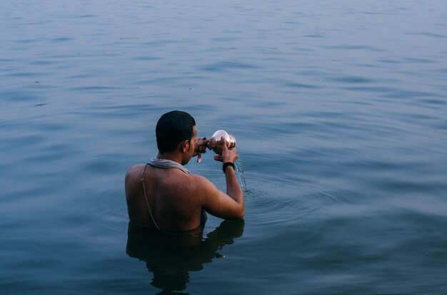 Person, die im Wasser steht, während die Kupferschale in Indien geleert wird
