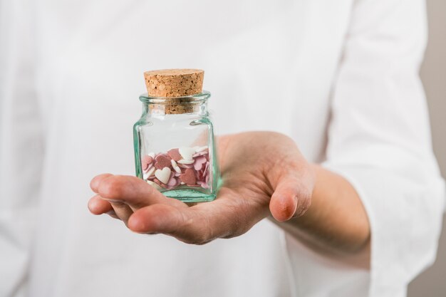 Person, die kleines Glas mit dekorativen Herzen hält