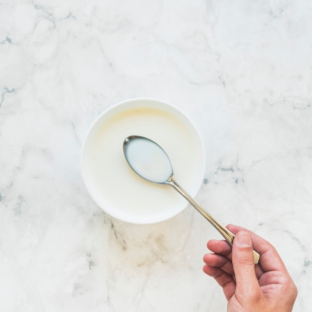 Person, die Löffel mit Milch über Schüssel hält