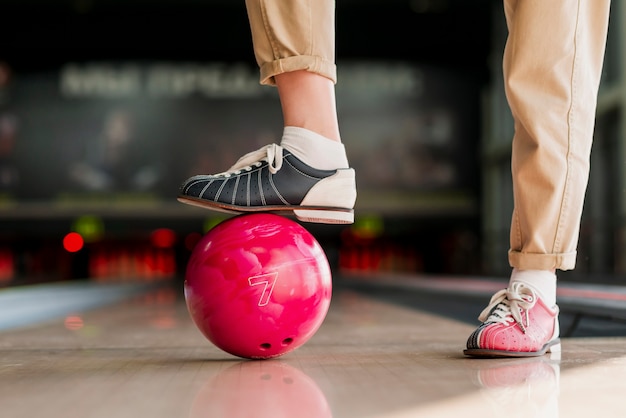 Person, die mit dem Fuß eine rote Bowlingkugel hält