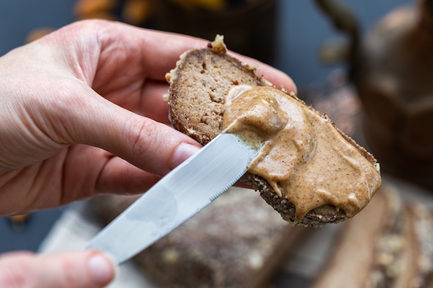 Person, die mit einem Messer Mandelcreme auf ein veganes Brot aufträgt