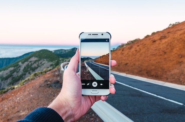Person, die mit seinem Telefon ein Bild von einer Straße auf einem Hügel macht - ideal für Tapeten