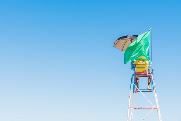 Person, die mit wehender grüner Flagge auf dem Sicherheitssitz am Strand steht