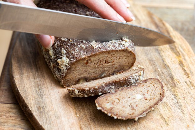 Person, die rohes veganes Brot mit einem Messer schneidet