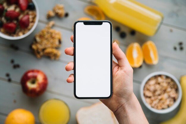 Person, die Smartphone mit leerem Bildschirm über Tabelle mit Früchten hält