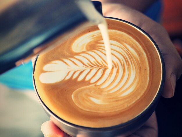 Person gießt Milch in eine Tasse Kaffee