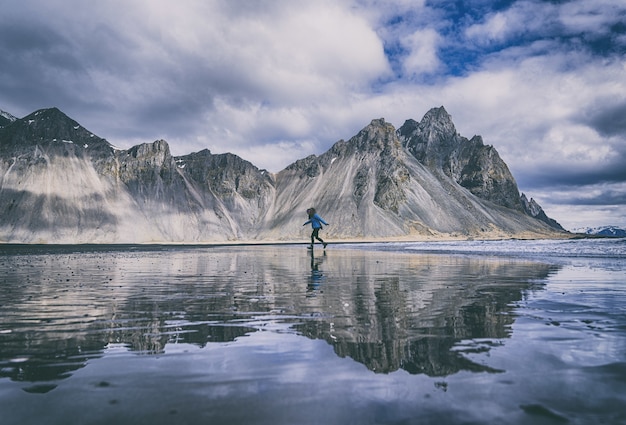 Person im blauen Hemd und in der schwarzen Hose, die auf blauem Kajak auf See nahe Berg unter steht