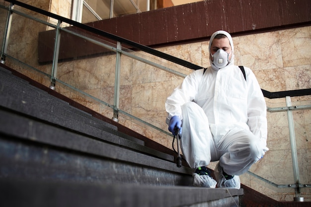 Person im weißen chemikalienschutzanzug desinfiziert öffentliche korridore und schritte, um die ausbreitung des hoch ansteckenden koronavirus zu stoppen