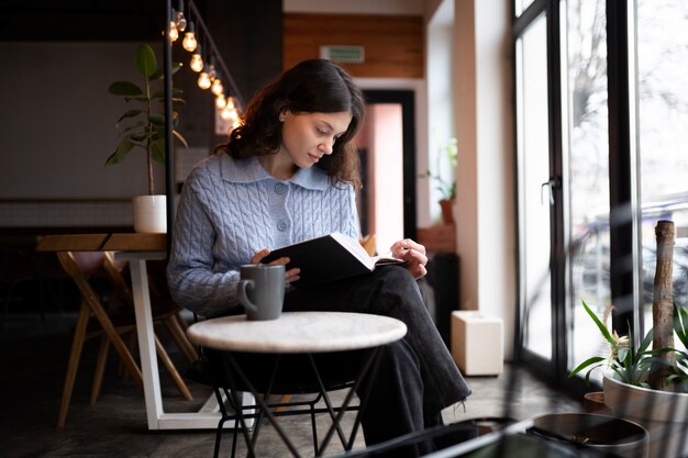 Kostenloses Foto person in einem café, die ein buch liest, während sie kaffee trinkt