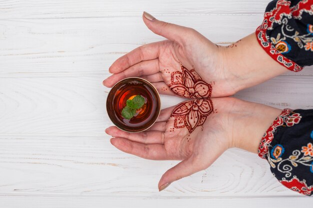 Person mit Mehndi hält eine kleine Tasse Tee