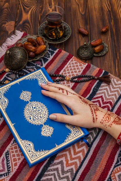 Person mit mehndi Quran in der Nähe von Tee und Dattelfrucht halten