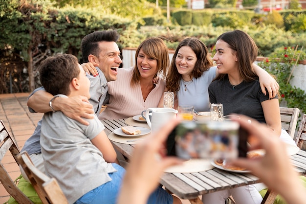 Person mit Smartphone, die ein Foto von der Familie macht, die zusammen im Freien zu Mittag isst