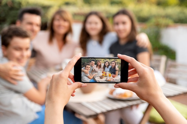 Person mit Smartphone, die ein Foto von der Familie macht, die zusammen im Freien zu Mittag isst