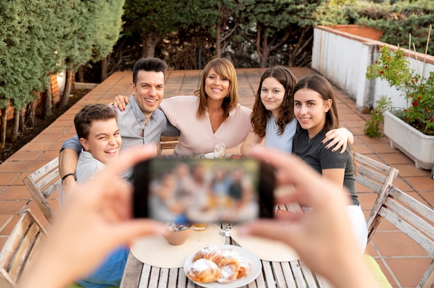 Person mit Smartphone, die ein Foto von der Familie macht, die zusammen im Freien zu Mittag isst