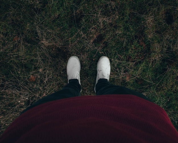 Person mit weißen Schuhen, die auf dem Rasen steht