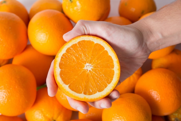 Person zeigt geschnittene orange Hälfte über Stapel von Früchten