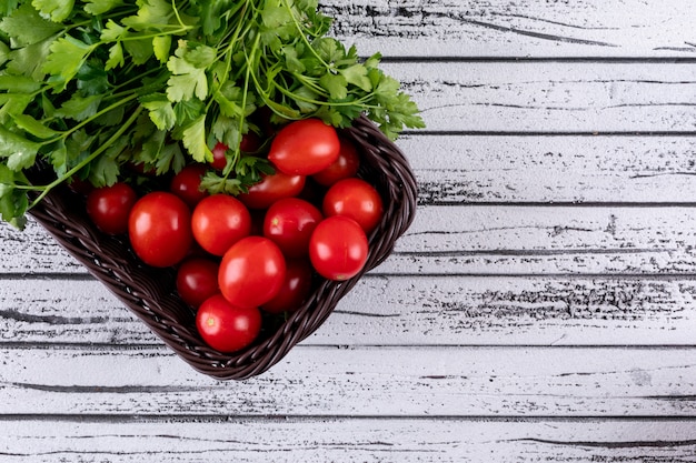 Kostenloses Foto petersilie und rote tomate im braunen gemüsekorb auf weißer holzoberfläche