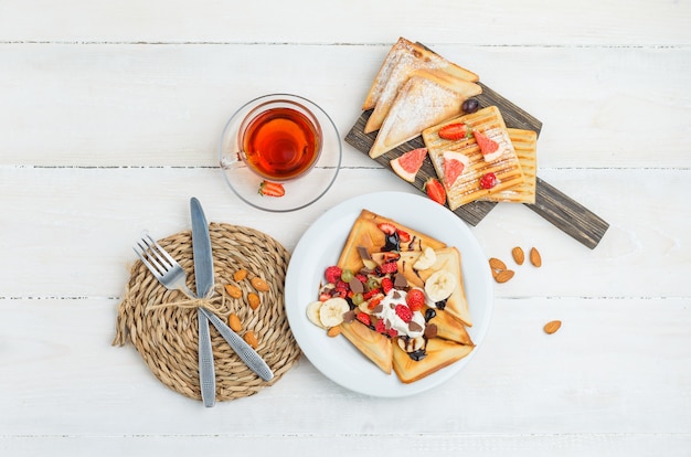 Pfannkuchen auf Holzbrett mit Tee, Mandeln, Messer, Gabel, Trauben und Himbeeren