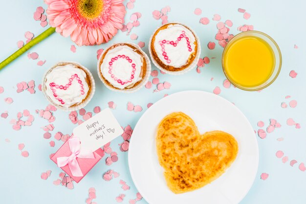 Pfannkuchen auf Platte in der Nähe von Blumen, Glas, Geschenk mit Tag und Kuchen mit Mutter Worten