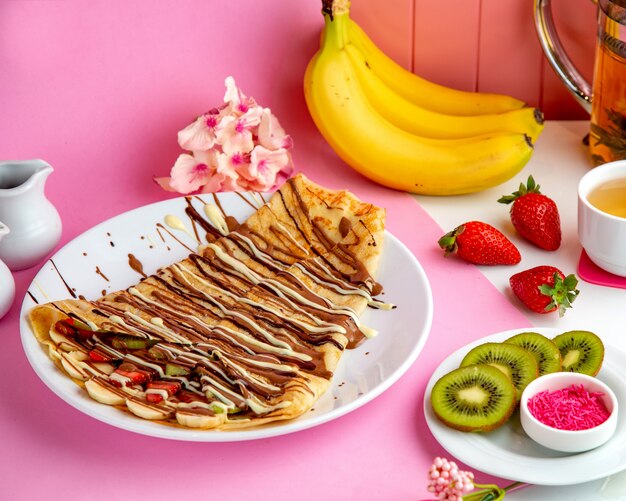 Pfannkuchen-Crepes mit Schokoladen-Bananen-Erdbeere und Kiwi auf dem Tisch