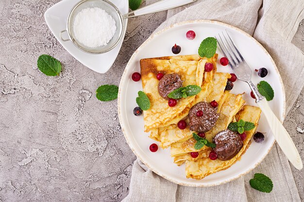 Pfannkuchen mit Beeren und Schokolade mit Minzblatt verziert. Leckeres Frühstück. Draufsicht