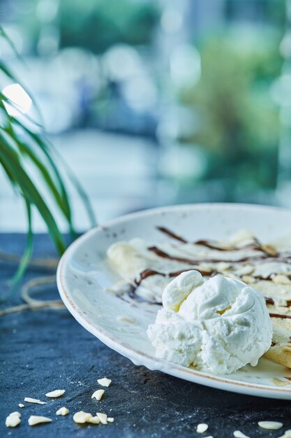 Pfannkuchen mit Eis, Streuseln, Schokolade auf dem weißen Teller in der dunklen Oberfläche